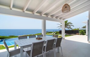 A covered outdoor dining area with a view of the ocean, a pool, and a patio with lounge chairs. - Beautiful home in Cala dOr with private swimming pool, can be inside or outside (Cala dOr)