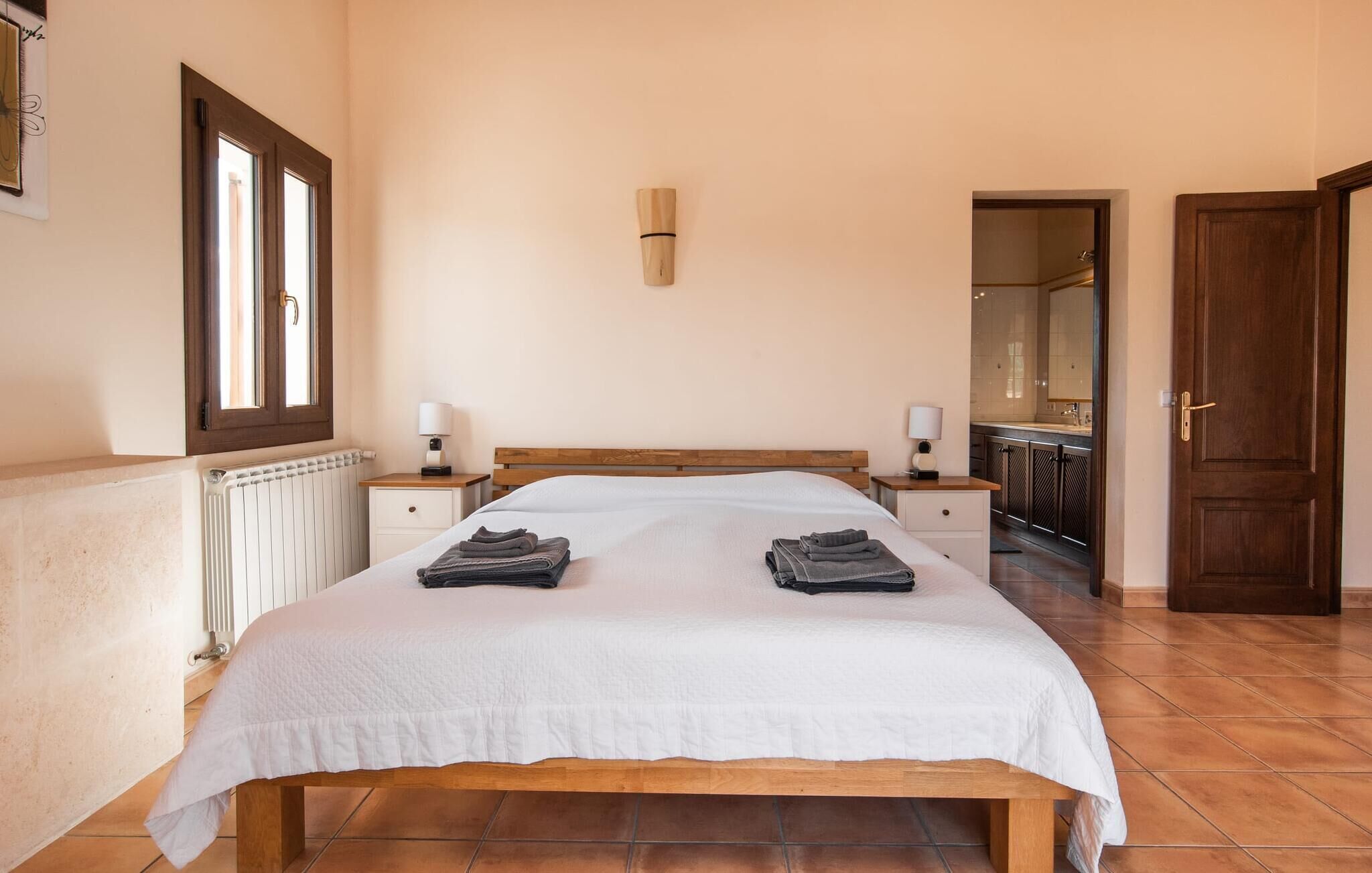 A bedroom with a wooden bed, two bedside tables with lamps, a radiator, and a bathroom visible through an open door.