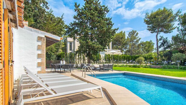 A swimming pool with sun loungers, a table with chairs, and a garden area with trees and flowers. - Lovely home in Alcudia with private swimming pool, can be inside or outside (Alcudia)