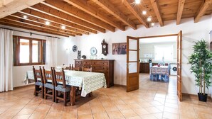 A dining area with a wooden table and chairs, a kitchen in the background, and a potted plant. - Beautiful home in Alcudia with private swimming pool, can be inside or outside (Alcudia)