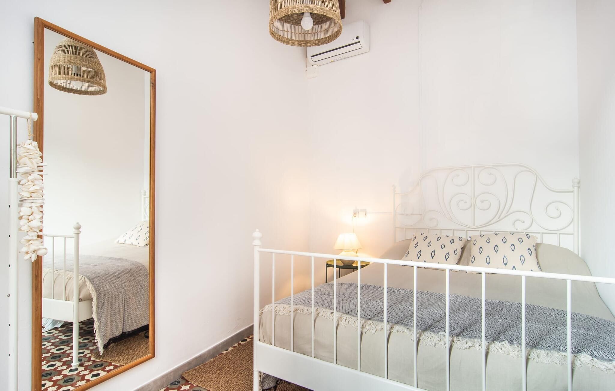 A bedroom with a white bed, a bedside lamp, a mirror, and a wicker lamp on the wall.