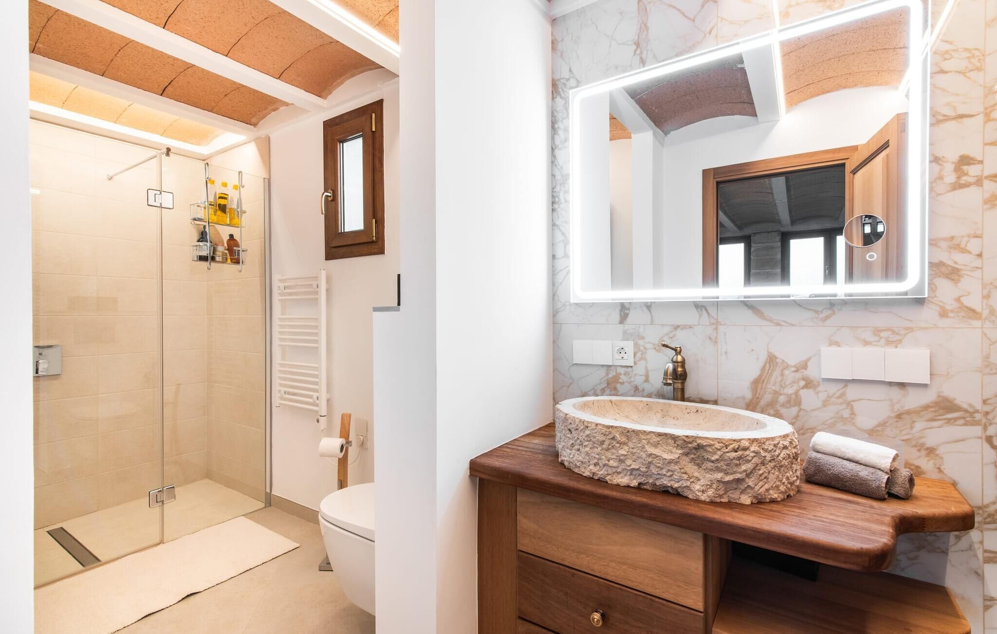 Une salle de bain avec un meuble-lavabo en marbre, un lavabo encastré, des toilettes et un espace douche.