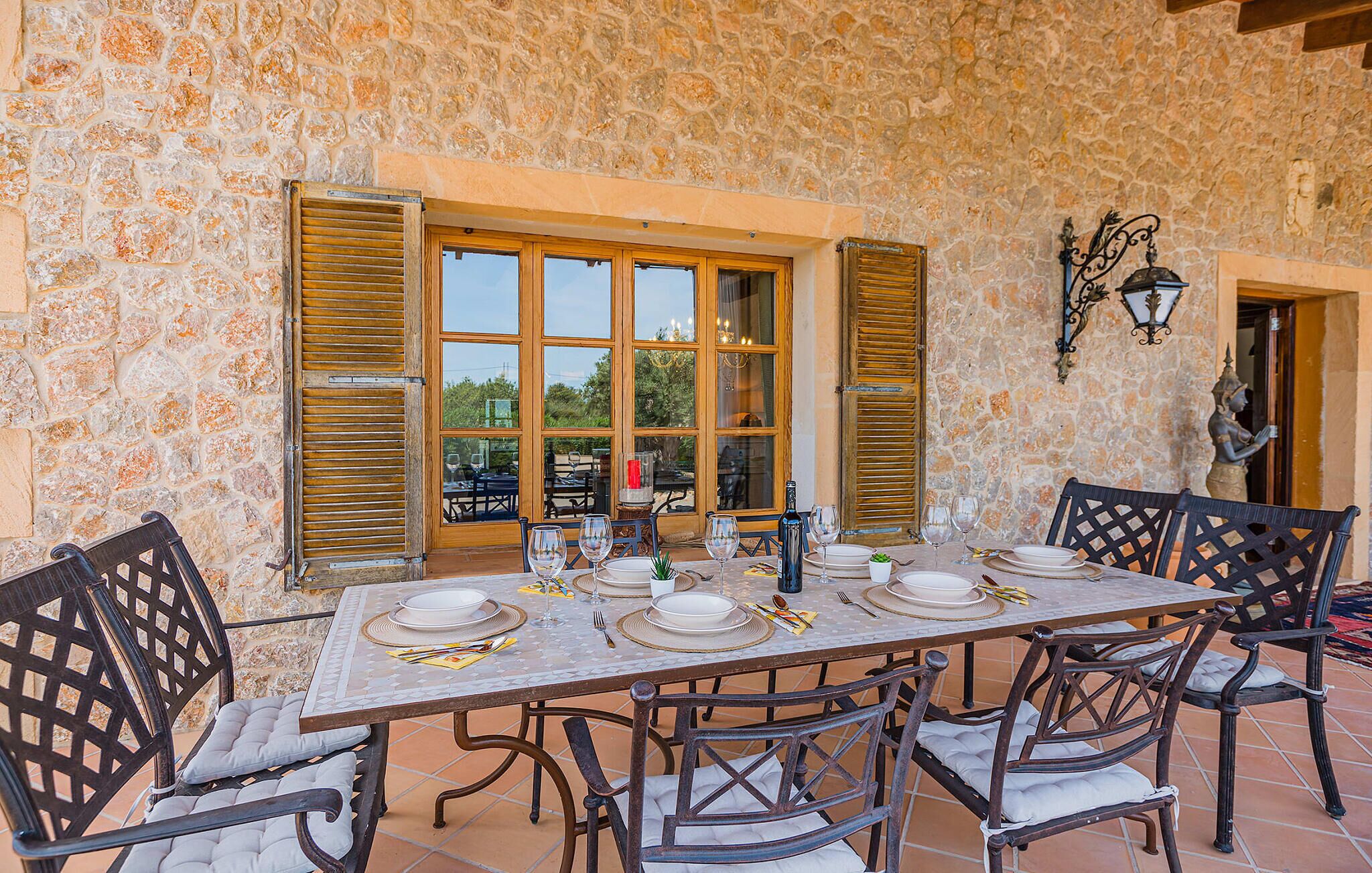 A dining area with a stone wall, wooden shutters, and a table set for six with chairs.