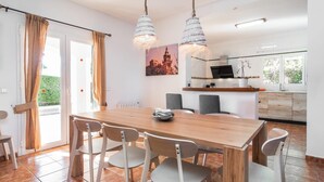 Ein Essbereich mit Holztisch und -stühlen, im Hintergrund eine Küche und Blick auf Grünfläche.