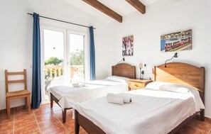 A hotel room with two beds, a wooden chair, a balcony with blue curtains, and a painting of a train on the wall. - Awesome home in Sa Rapita with private swimming pool, can be inside or outside (Sa Rapita)