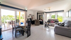 A spacious living room with a dining area, a sofa, and a coffee table. There are large windows providing natural light and a view of greenery outside. - Amazing home in Sa Coma with private swimming pool, can be inside or outside (Sa Coma)