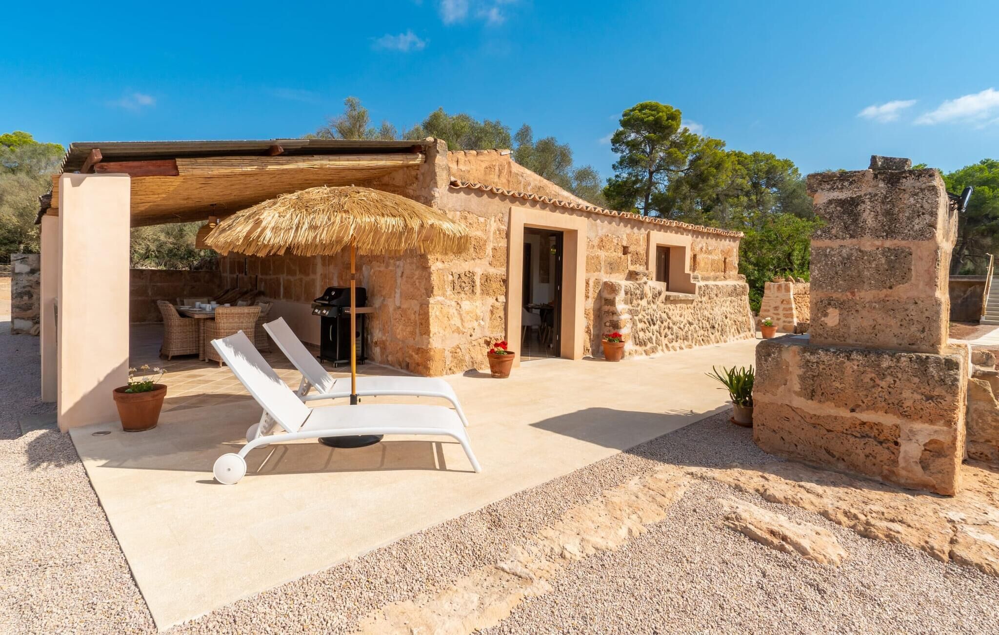 Um edifício de pedra com terraço e telhado de palha, área de estar ao ar livre e piscina.