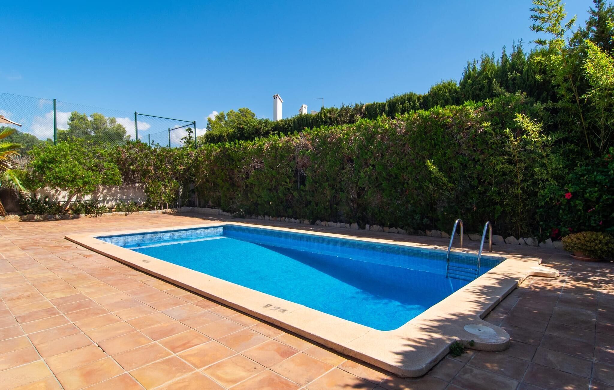 A rectangular swimming pool with a tiled edge, surrounded by a tiled patio area.