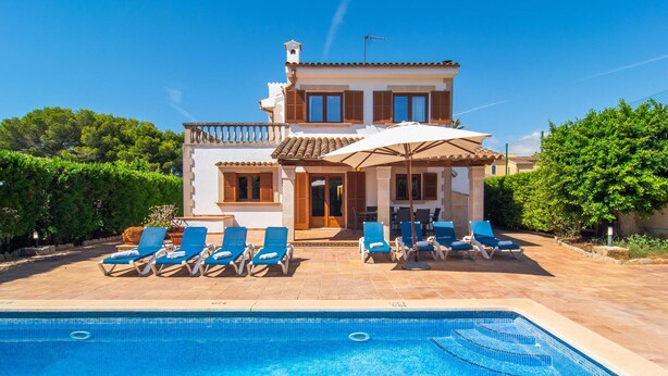 Eine zweistöckige Villa mit Pool, Sitzgelegenheiten im Freien und einer überdachten Terrasse.