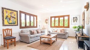 Ein geräumiges Wohnzimmer mit zwei Sofas, einem Couchtisch und einem Holzstuhl. Große Fenster sorgen für natürliches Licht, und an den Wänden sind Kunstwerke zu sehen.