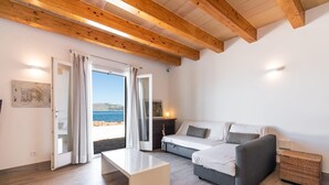 En moderne stue med træloft, sofa, sofabord og havudsigt gennem en glasdør.