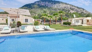 A swimming pool with lounge chairs, a stone building, and a mountain in the background. - Lovely home in Pollenca with private swimming pool, can be inside or outside (Pollenca)