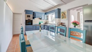 A modern kitchen with blue cabinets, a glass dining table, and a view of the outdoors. - Lovely home in Pollenca with private swimming pool, can be inside or outside (Pollenca)