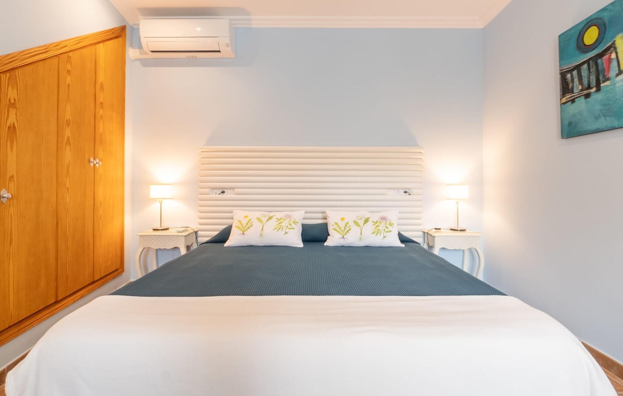 Un dormitorio con cama, lámparas de noche, un armario de madera y un aire acondicionado instalado en la pared.