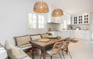 A modern kitchen with white cabinets, a wooden dining table, wicker chairs, and two hanging wicker light fixtures. - Cozy home in Palma with private swimming pool, can be inside or outside (Palma)