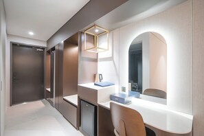 Een moderne hotelkamer met een bureau, een stoel, een kastje, een spiegel en een deur.