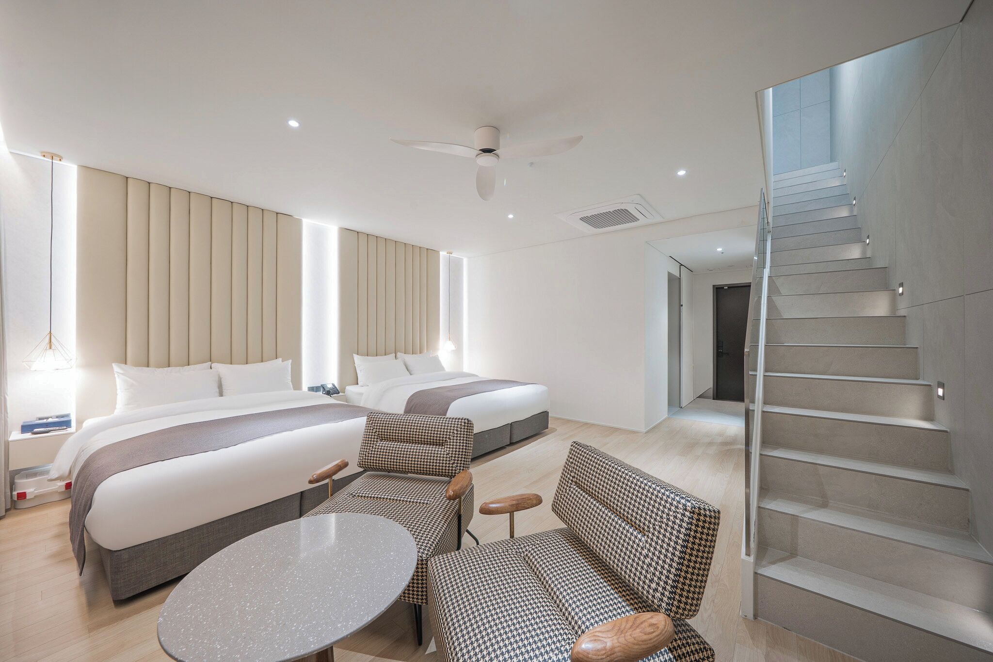Una habitación de hotel moderna con una cama grande, dos mesitas de noche, una mesa redonda y una escalera.