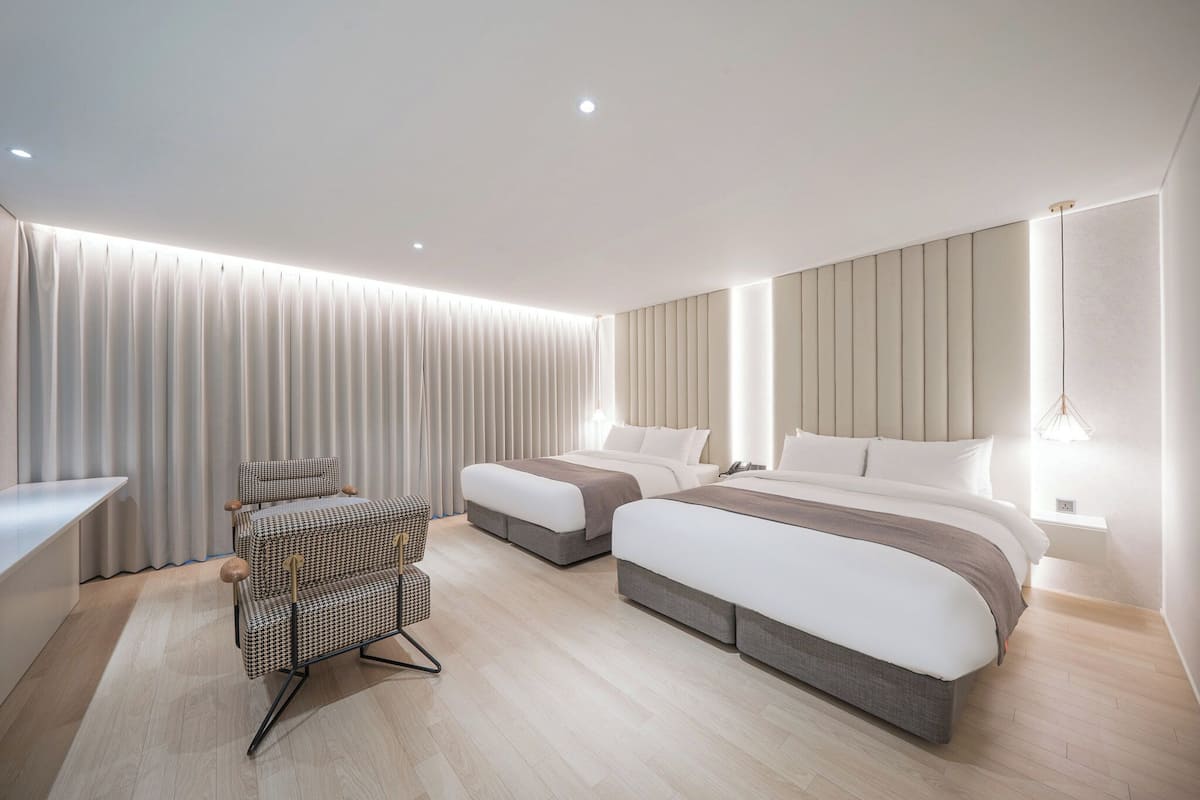 A modern hotel room with two beds, a seating area, and a desk.