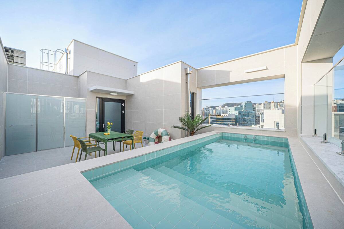 A rooftop pool with a table and chairs, a small plant, and a city view.