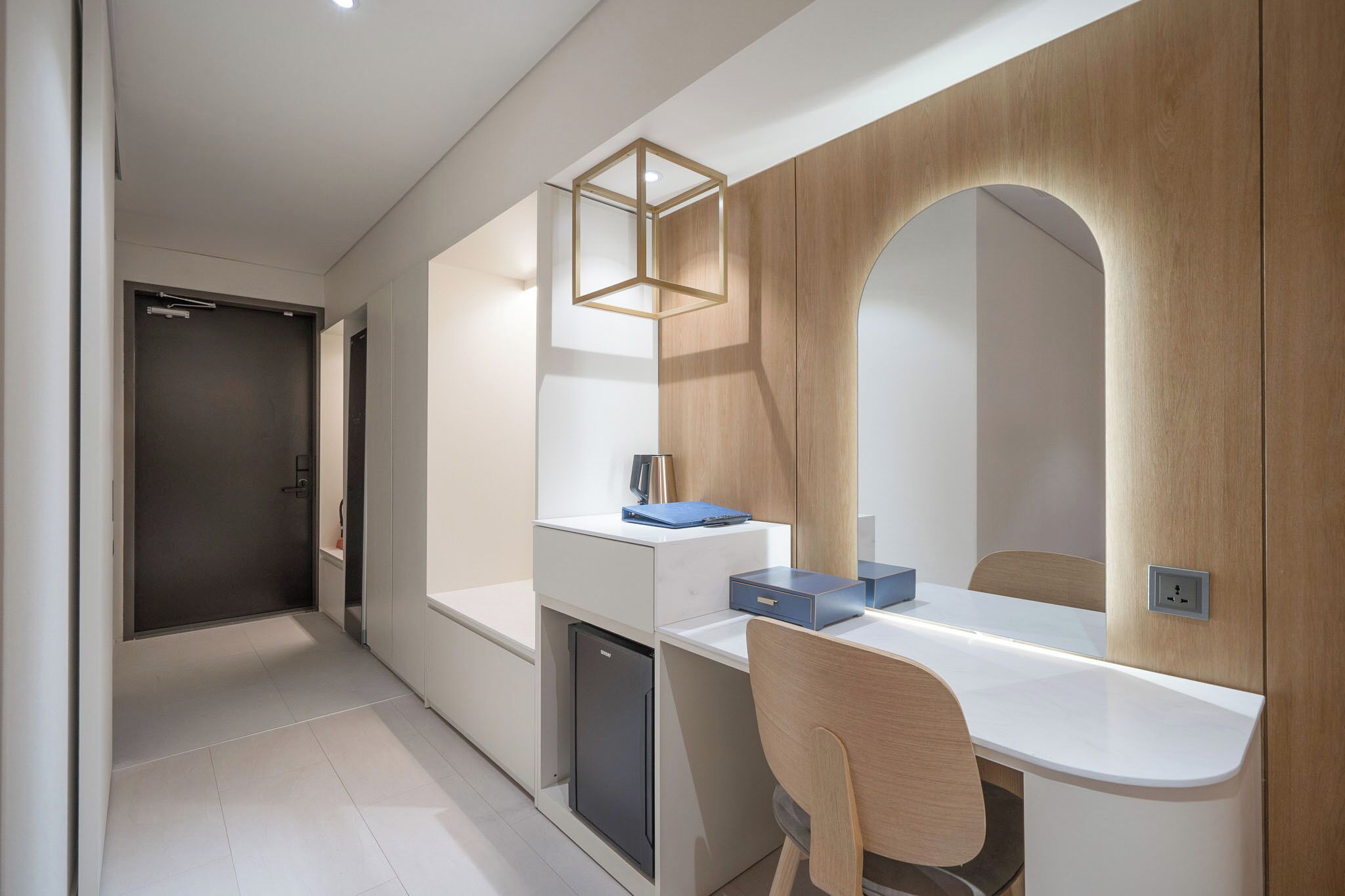 A modern hotel room with a white desk, a mirror, a small cabinet, and a door.