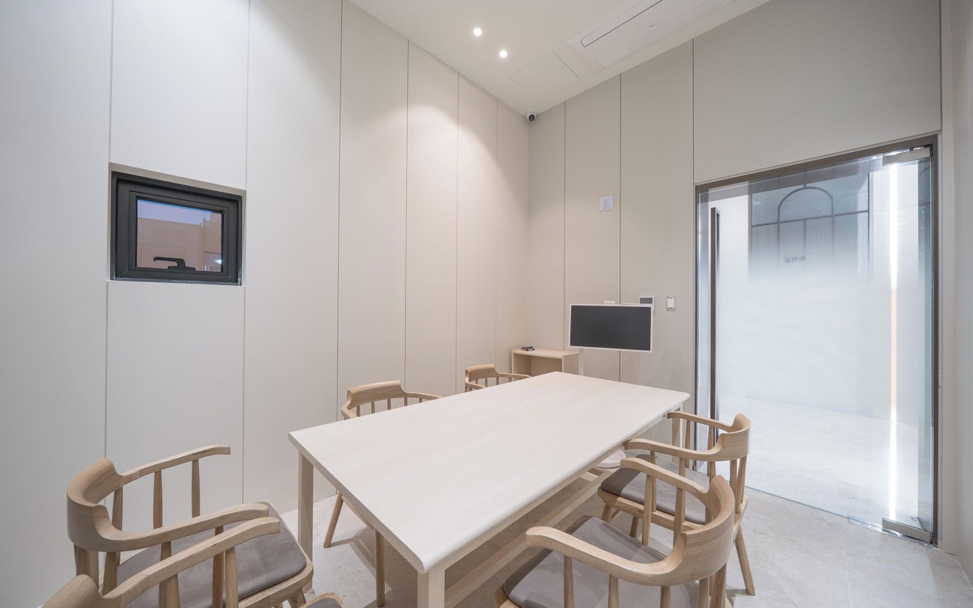 A conference room with a long table and six chairs, a flat-screen TV, and a door leading to another room.