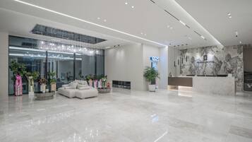 A modern hotel lobby with a reception desk, seating area, and a large window with decorative lights.