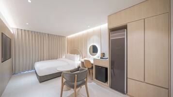 Et moderne hotelværelse med seng, skrivebord, stol og indbygget køleskab.