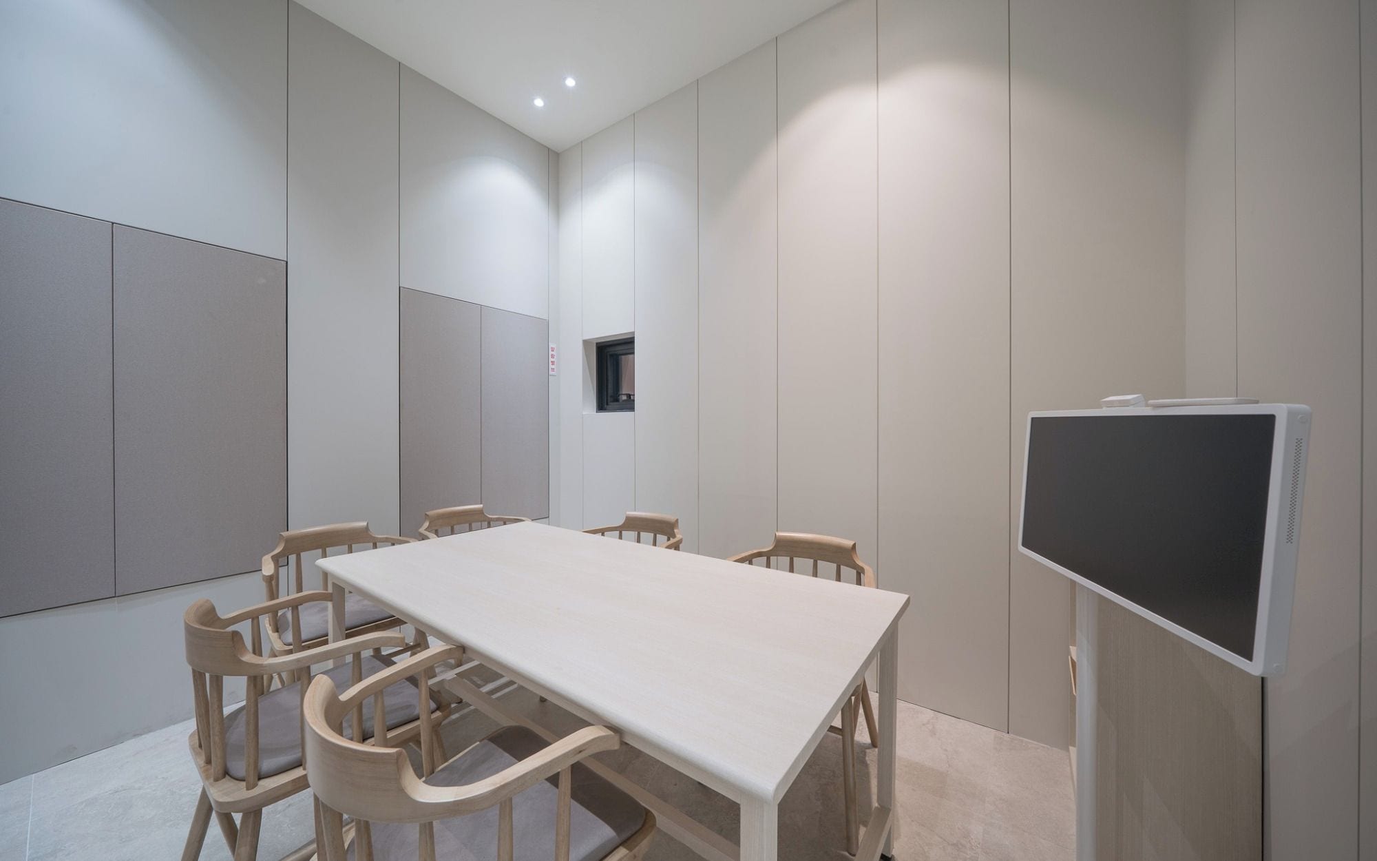 Un salón de conferencias con una larga mesa, seis sillas, un televisor y un ventanal pequeño.