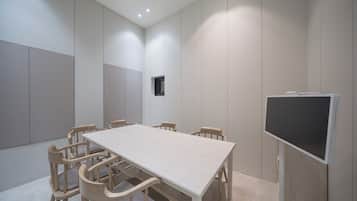Un salón de conferencias con una larga mesa, seis sillas, un televisor y un ventanal pequeño.