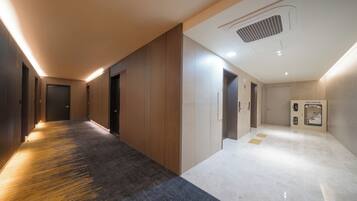 A hallway with a carpeted floor, wooden walls, and a ceiling vent.
