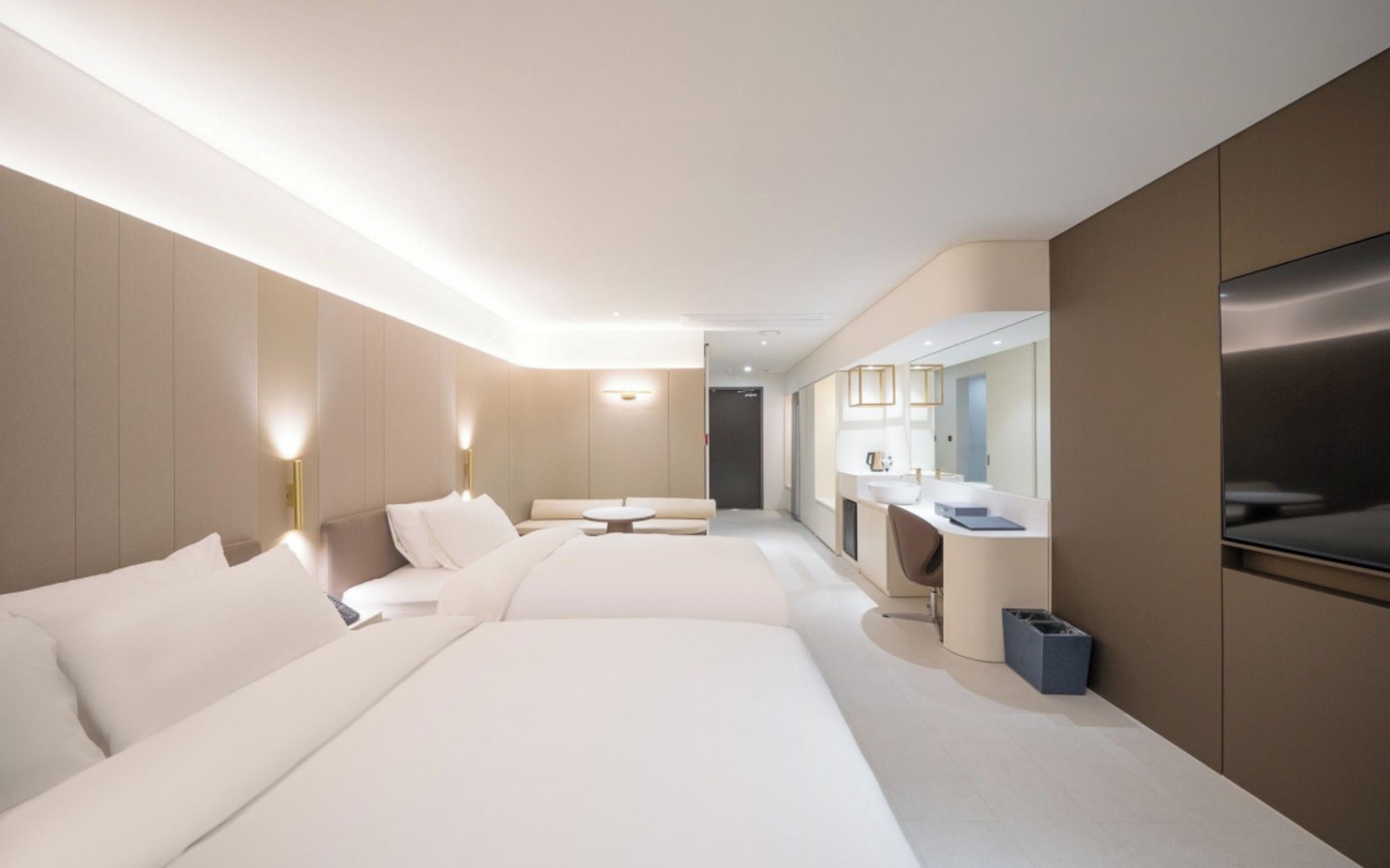 A modern hotel room with two beds, a sitting area, a large mirror, and a television.