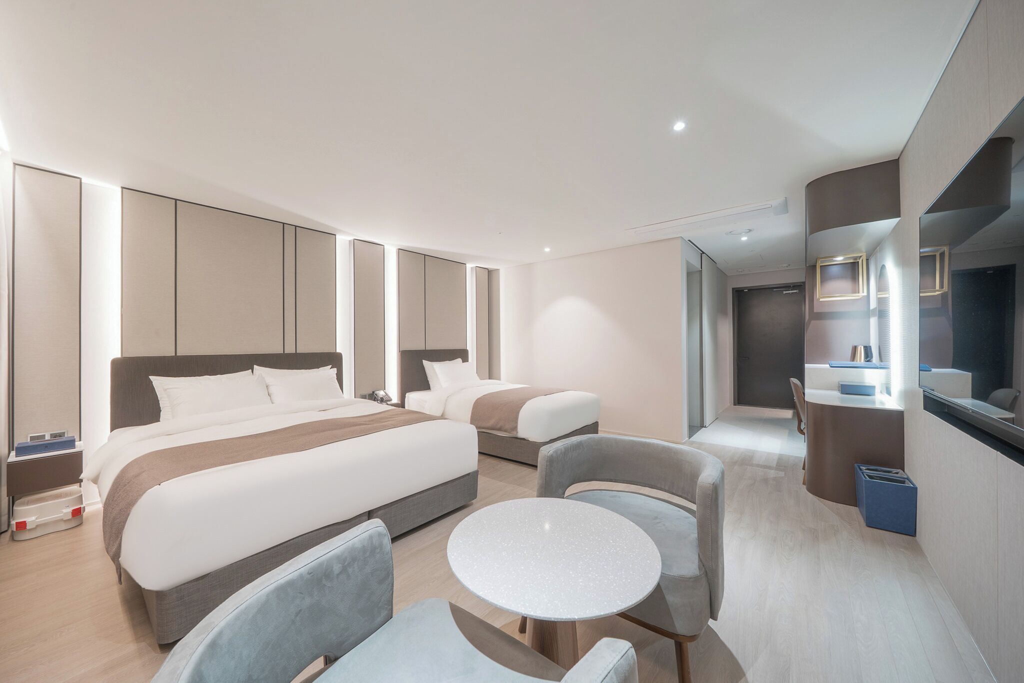 Una habitación de hotel moderna con dos camas, una mesa redonda y un escritorio pequeño.