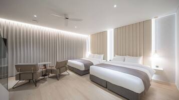 A modern hotel room with two beds, a seating area, and a ceiling fan.