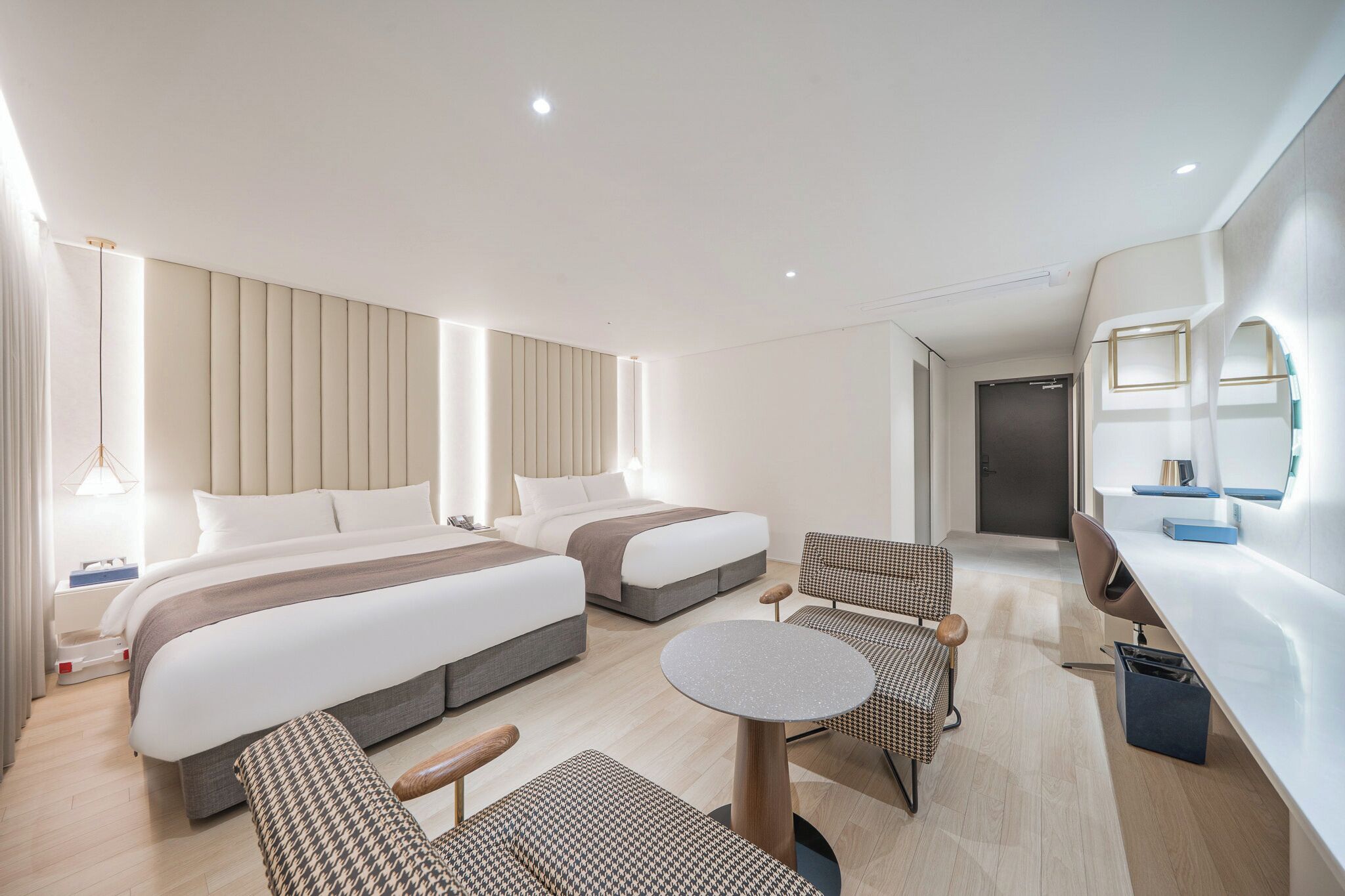 A modern hotel room with two beds, a desk, a chair, and a small table.