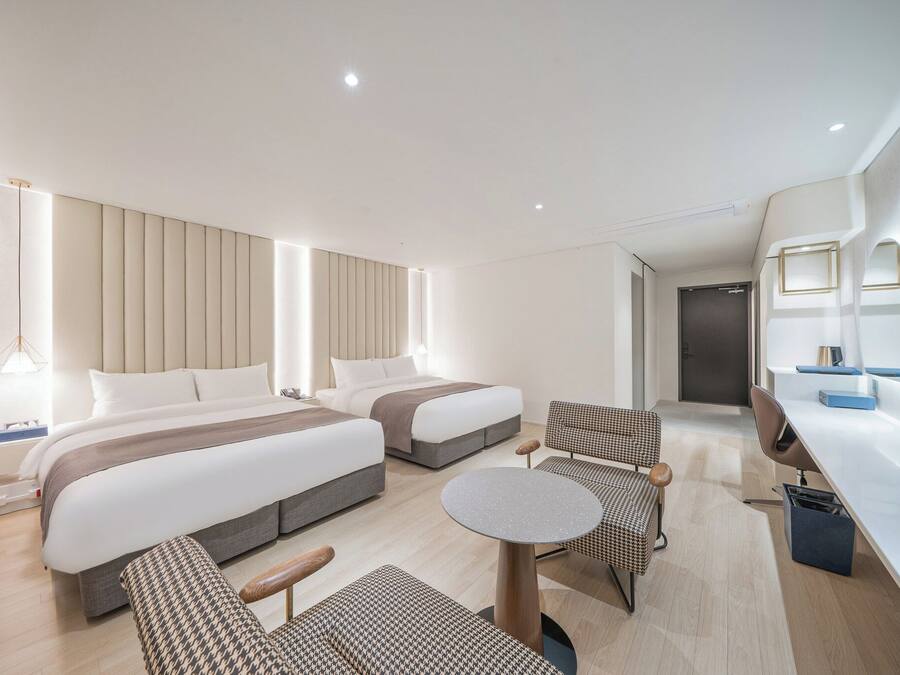 A modern hotel room with two beds, a desk, a chair, and a small table.