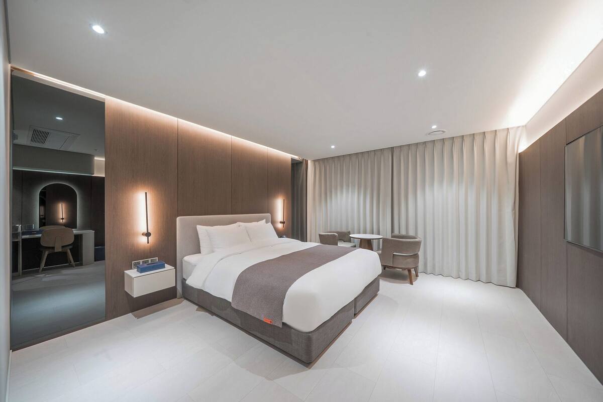 A modern hotel room with a large bed, bedside tables, a desk, and a seating area.