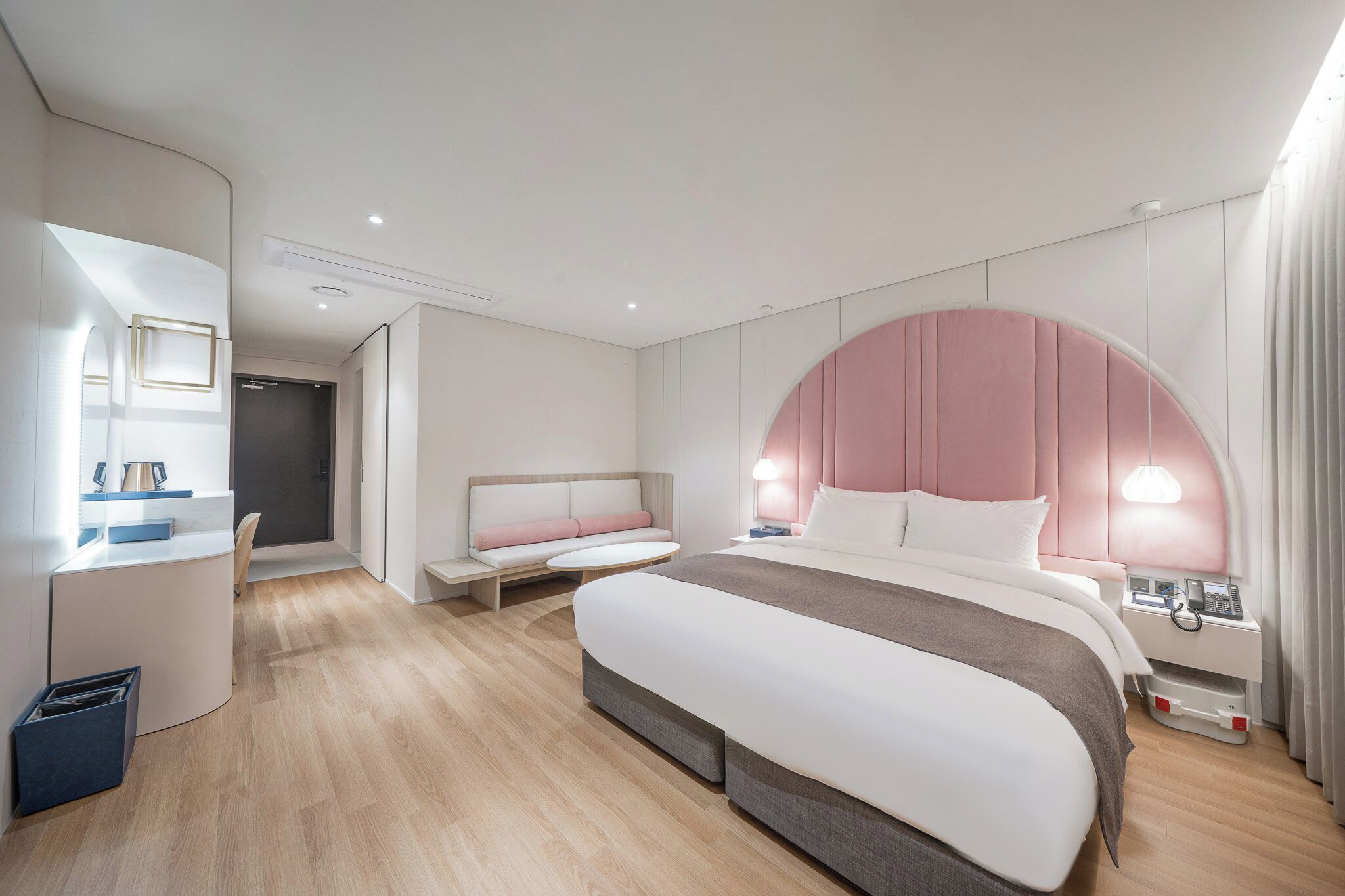 A modern hotel room with a large bed, a desk, a seating area, and a vanity.