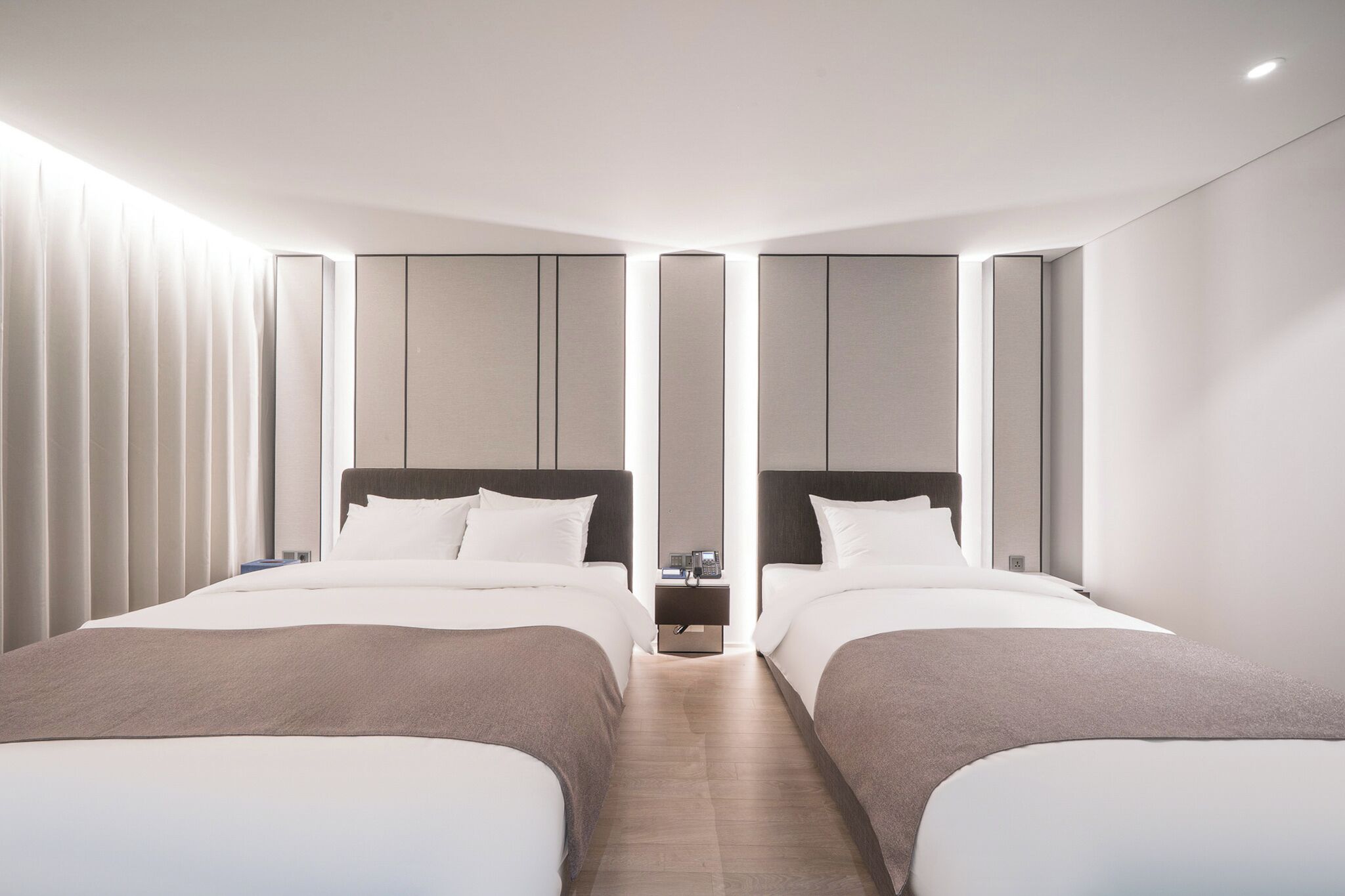 A modern hotel room with two beds, a nightstand, and a wall-mounted phone.