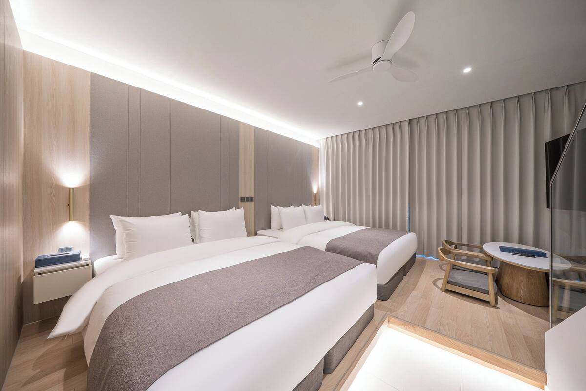 A modern hotel room with two beds, a desk, and a chair.
