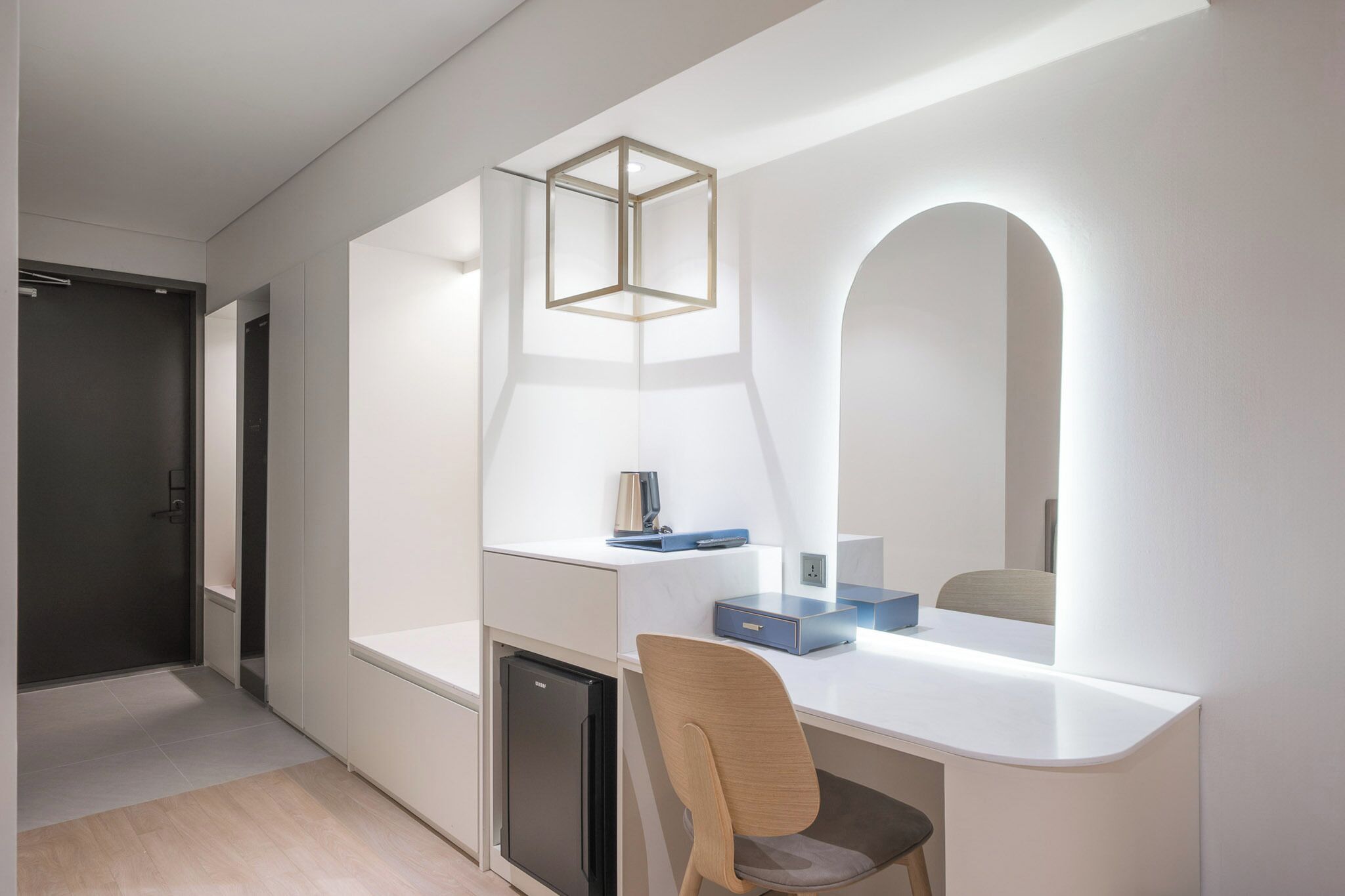 Una habitación moderna y minimalista con un escritorio blanco, una silla, un mueble pequeño y un espejo con marco arqueado.