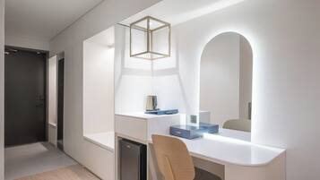 Una habitación moderna y minimalista con un escritorio blanco, una silla, un mueble pequeño y un espejo con marco arqueado.