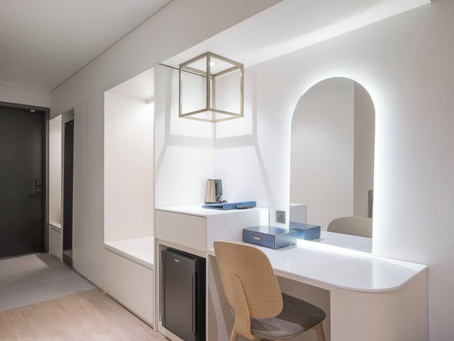 Una habitación moderna y minimalista con un escritorio blanco, una silla, un mueble pequeño y un espejo con marco arqueado.