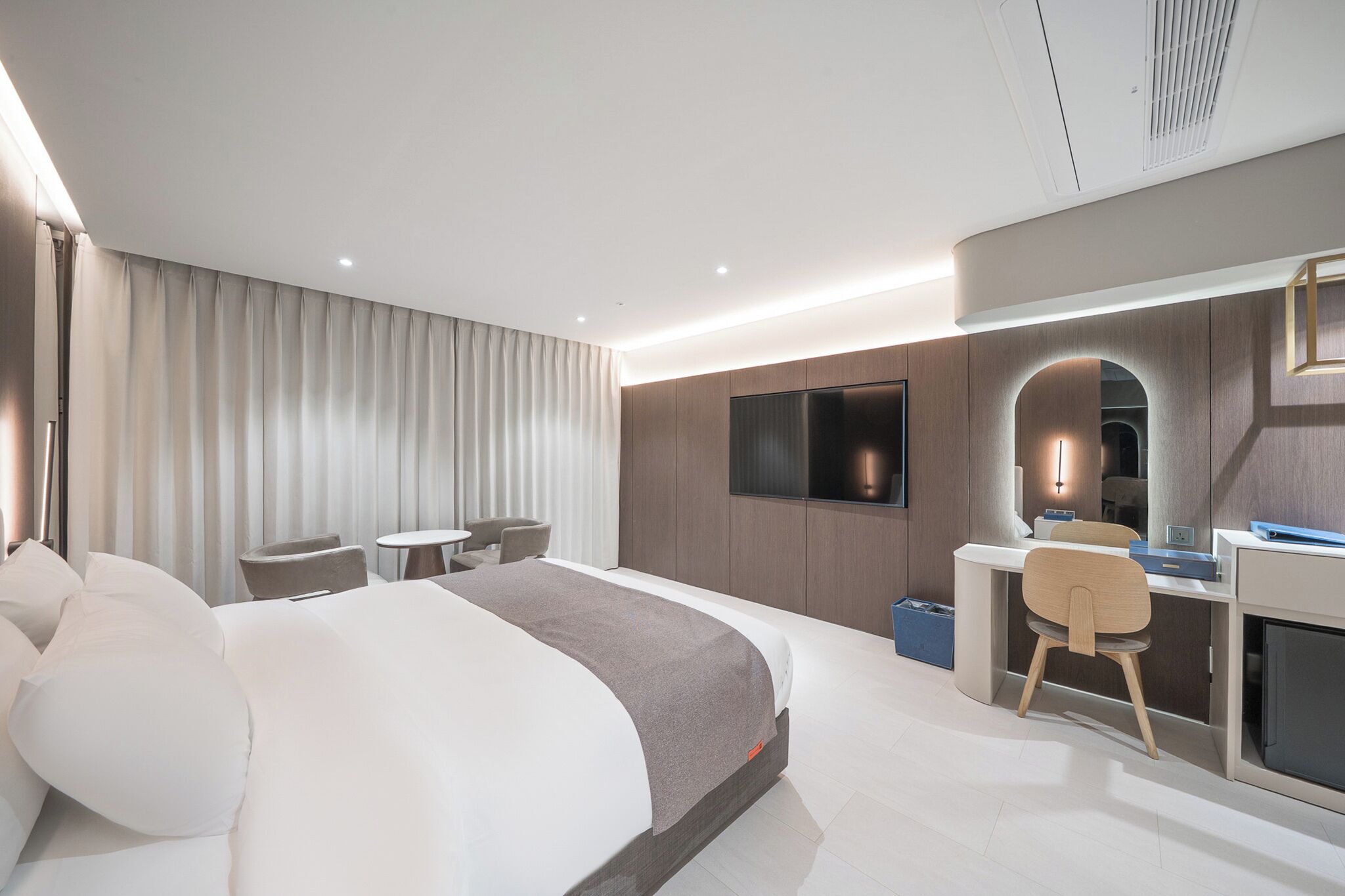 Una habitación de hotel moderna con una cama grande, un escritorio, una silla, un televisor y un espejo.