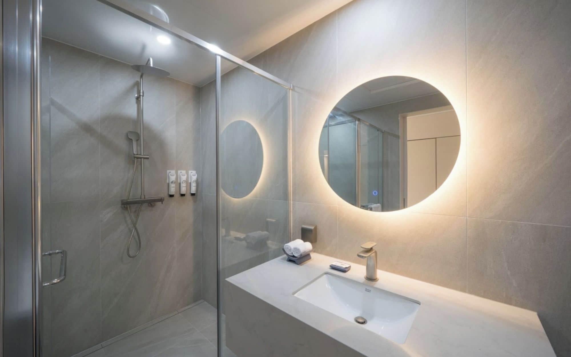 A modern bathroom with a glass-enclosed shower, a large mirror, and a white sink.