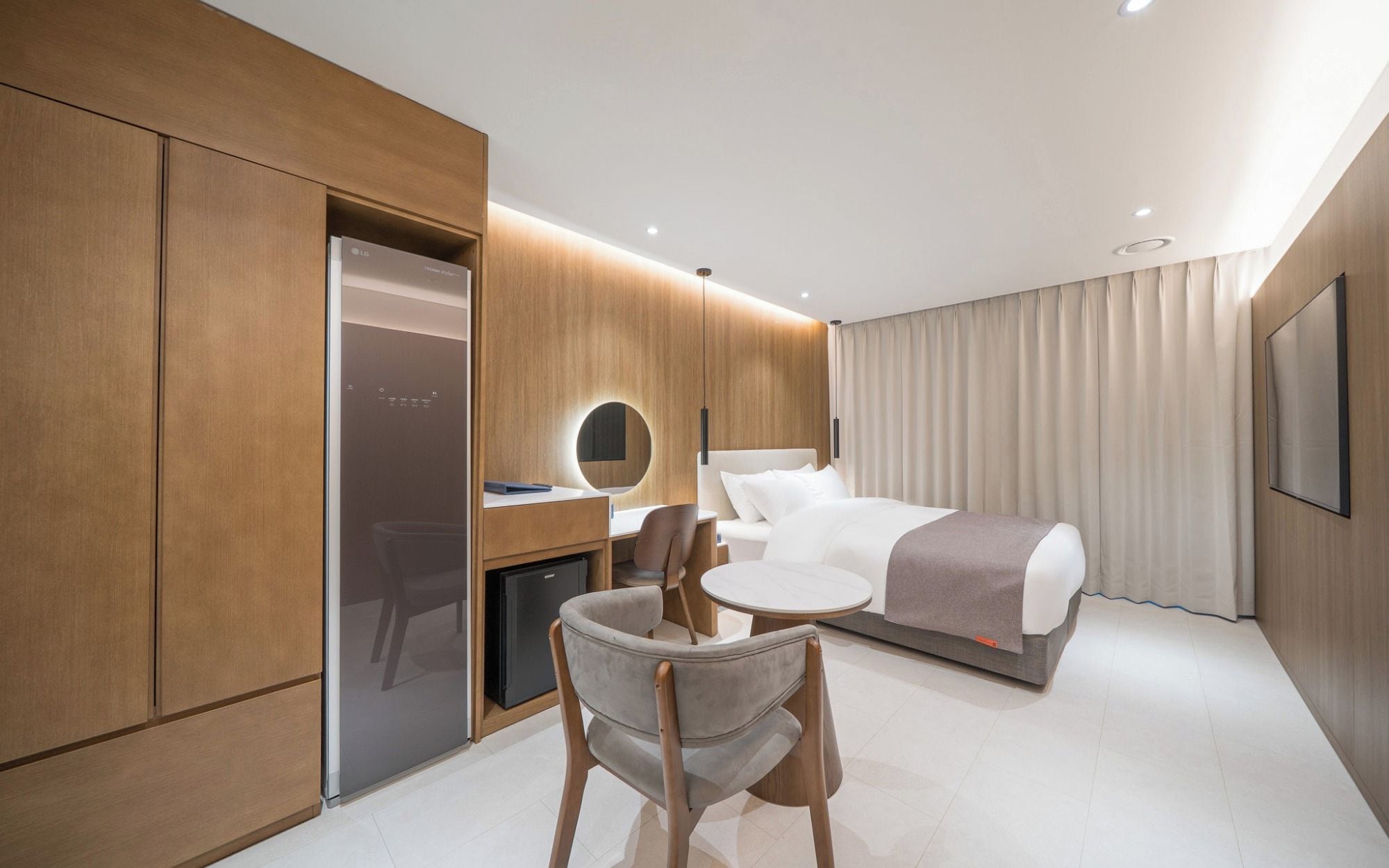 A modern hotel room with a bed, bedside table, chair, desk, and a built-in wardrobe.