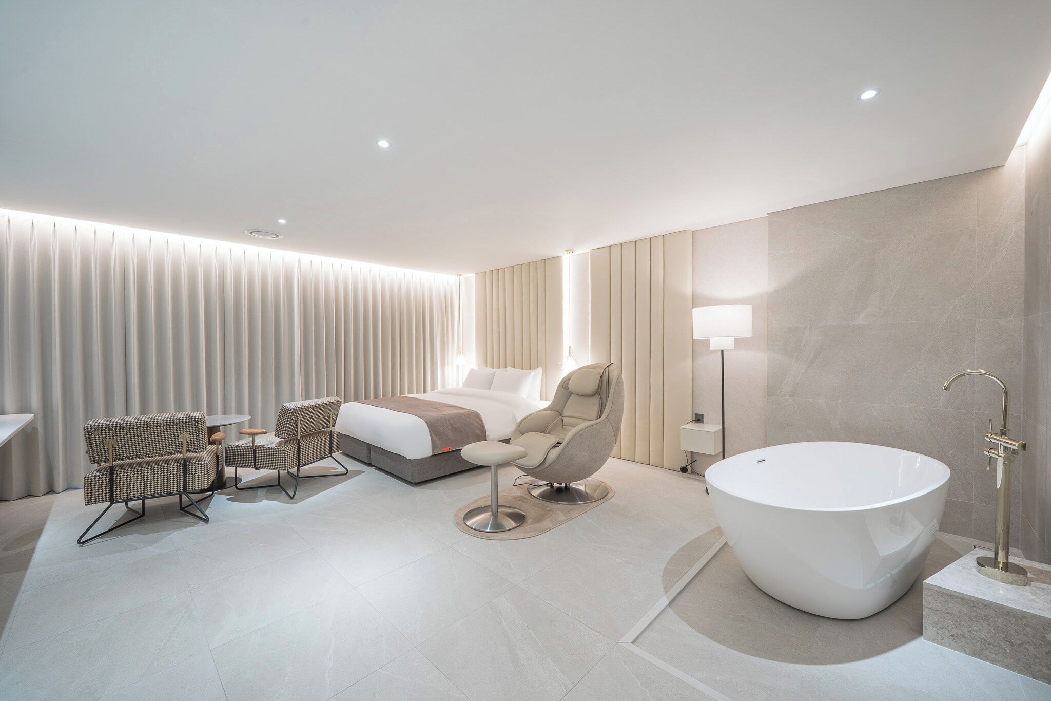 A modern hotel room with a large bathtub, a bed, a sofa, and a small table.