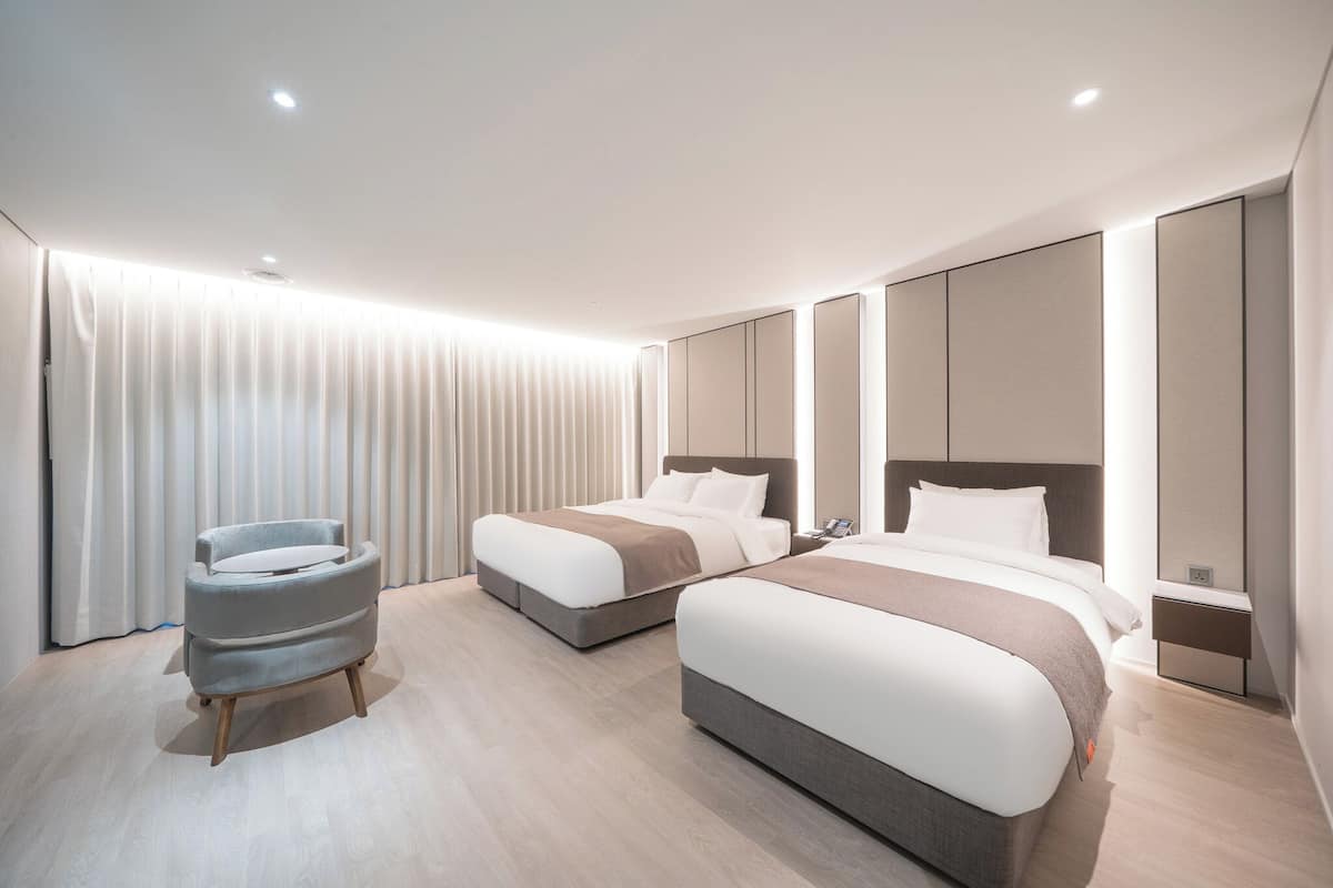 A modern hotel room with two beds, a seating area, and a large window with curtains.