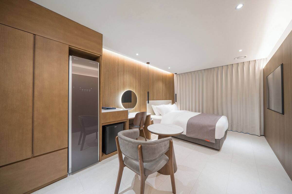A modern hotel room with a bed, a desk, a chair, and a television.