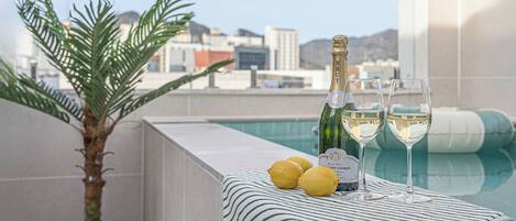 A rooftop pool area with a bottle of champagne, two glasses, and lemons on a towel.