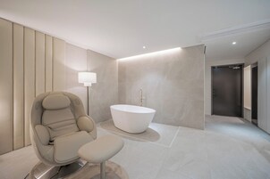 Un baño moderno con una bañera independiente, una silla de masaje y una lámpara de pie.